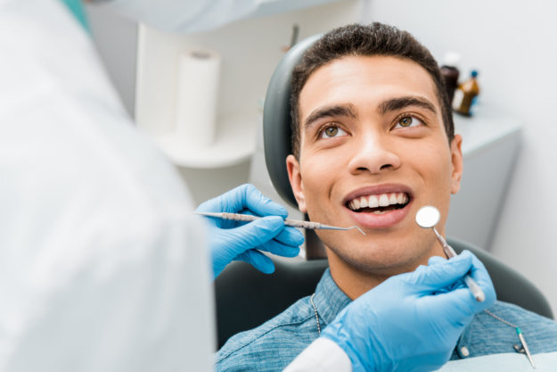 cheerful african american man with during examination in dental clinic man getting dental sealants