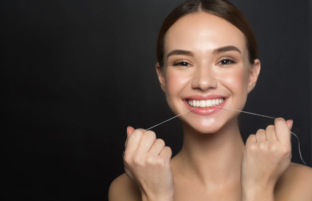 Contented girl is using special interdental thread young woman flossing and smiling after teeth grinding treatment